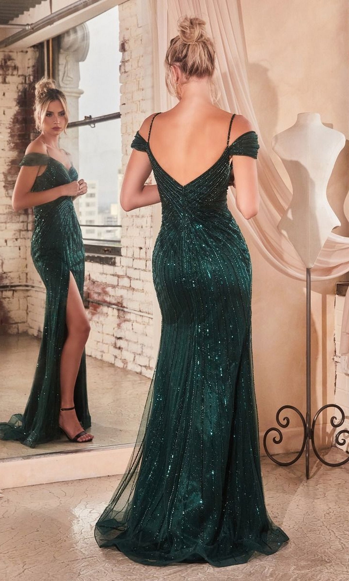 A woman in the Cold-Shoulder Long Sequin Prom Dress CD0219, featuring a dark green hue and thigh-high slit, stands before a mirror with her back reflected.